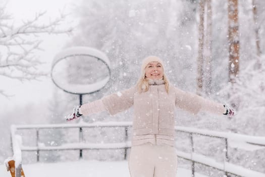 A cheerful woman stands under the snow in a winter forest.