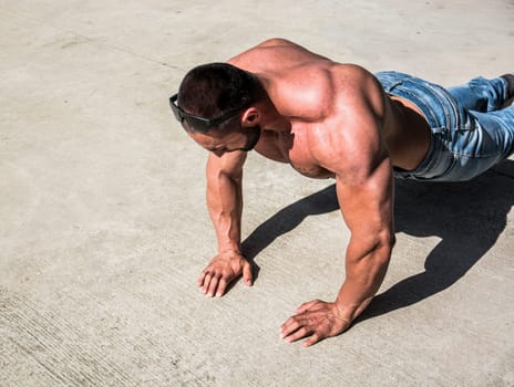 A shirtless man is doing push ups on concrete