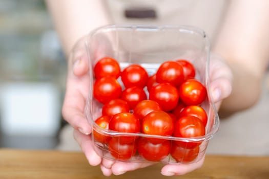 Woman's hands holding a box of cherry tomatoes close-up. Preparing cherry tomatoes for salad or side dish. High quality photo
