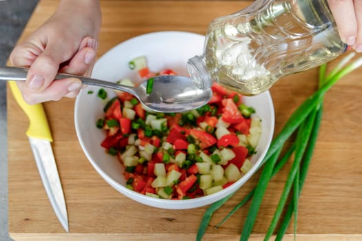 A woman's hands pour a couple of large spoons of oil, close-up, to make the salad juicier and tastier. High quality photo