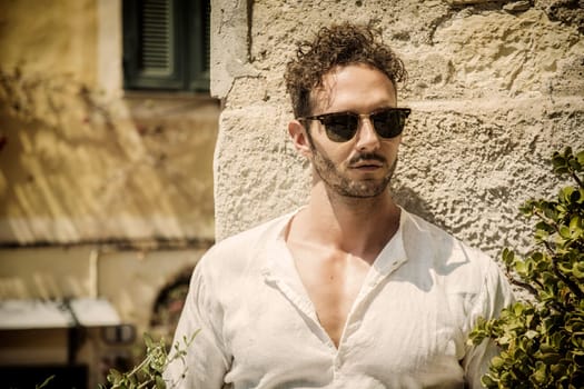 A man wearing sunglasses standing in front of a stone wall