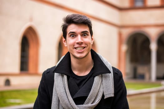 A man standing in front of a building with a scarf around his neck