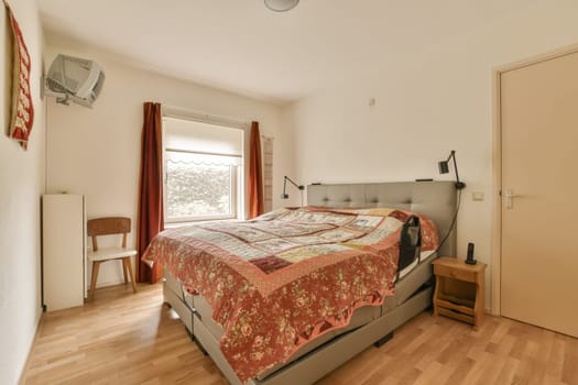 a bed in a room with wood flooring and red bedspreed sheets on the bed, next to a window
