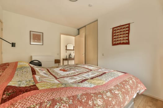 a bed with quilts on it in a room that has white walls and wood flooring around the headboard
