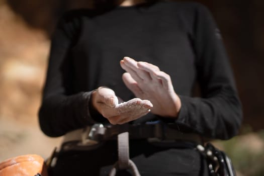 The girl is engaged in rock climbing, uses white powder of magnesia, claps her hands close-up, the woman leads an active lifestyle, climbs the mountains outdoor.