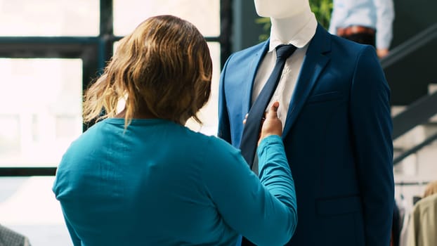 African american woman checking fashionable suit, analyzing tie fabric before buying it in clothing store. Shopaholic customer shopping for formal wear in modern boutique. Fashion concept