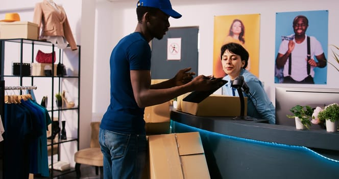 African american store courier discussing packages distribution with manager, showing shipping report in modern boutique. Stylish employee working at online orders, preparing boxes for delivery
