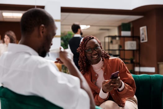 Happy people relaxing together on couch, waiting in lounge area before filling in registration forms at hotel front desk. Modern hotel guests sitting on sofa preparing to do room check in.