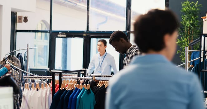 African american customer looking at hangers with trendy shirt, analyzing clothes fabric before buying it. Shopaholic man shopping for fashionable merchandise and accessories in modern boutique