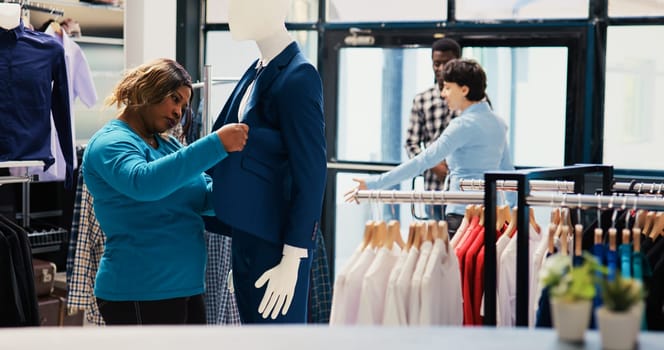 African american customer looking at elegant suit, analyzing merchandise fabric in modern boutique. Shopaholic woman shopping for fashionable clothes, buying trendy items in clothing store