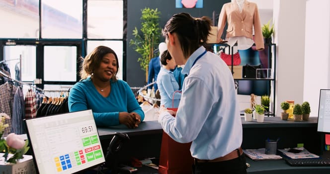 African american customer putting credit card on pos terminal paying for fashionable clothes at counter desk in modern boutique, Woman shopper buying trendy merchandise in clothing store