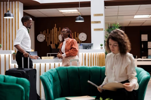 Tourists ringing bell at desk in lobby calling out hotel staff to help with booking registration process. Happy couple with trolley bags preparing to check in for room reservation, luxury resort.