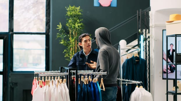 African american robber trying to sneak stolen shirt being caught by store security guard in modern boutique. Bodyguard asking thief to return stylish merchandise or will call the police