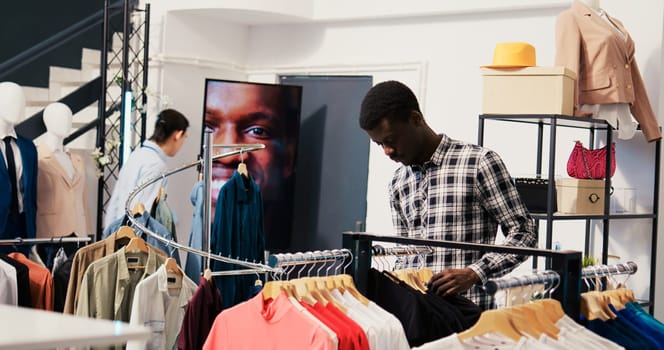 African american customer checking shirt fabric in modern boutique, wanting trendy clothes for new wardrobe. Shopaholic man shopping for fashionable merchandise in clothing store. Fashion concept