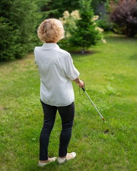 Rear view of an elderly blind woman walking in the park with a tactile cane