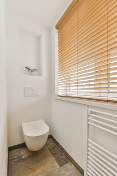 a white bathroom with wooden blinds on the window and toilet in the fore - image was taken from an interior shot