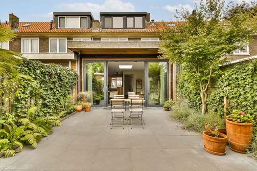 an outdoor dining area with plants and pots on the patio in front of a modern home surrounded by lush vegetation