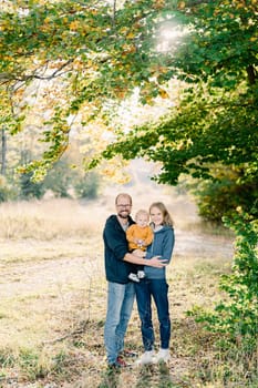 Mom and dad stand hugging with a little boy in their arms in the park. High quality photo