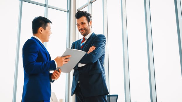 Two business people talk project strategy at office meeting room. Businessman discuss project planning with colleague at modern workplace while having conversation and advice on financial report. Jivy