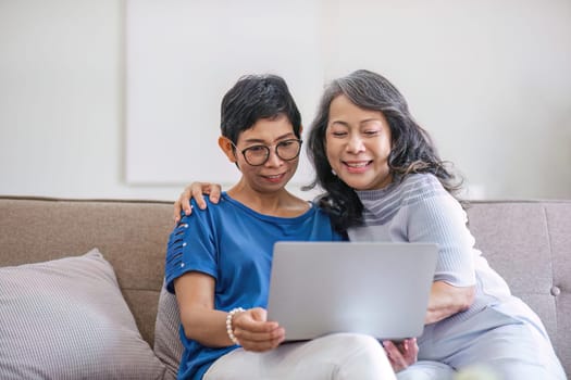 two 60s woman enjoy with social media on her laptop on a sofa.