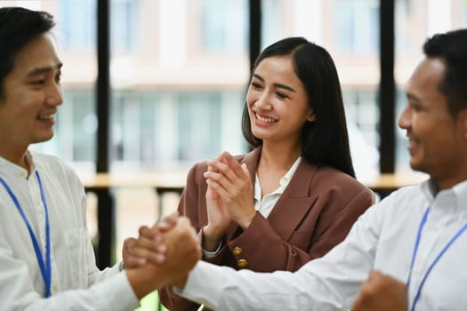 Smiling businesswoman clapping hands while businesspeople stacking hands showing team building or celebrate their unity in the office.