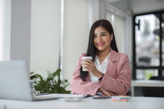 Businesswoman working with laptop computer while having a leisurely cup of coffee at the office in the morning..