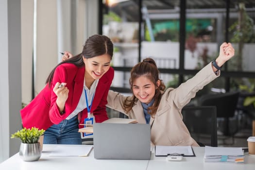 Two Asian businesswoman showing excited expression in front of laptop due to successful results..