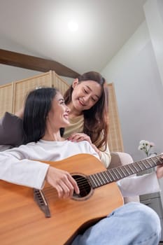 LGBT. Two young women play guitar and sing in the living room too together for a happy time..