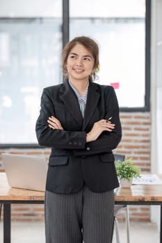 Portrait, Young confident smiling Asian business woman wearing suit standing in office with arms crossed..