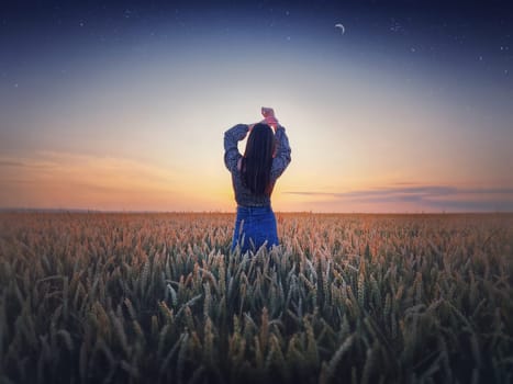 Girl in the golden wheat field at sunset. Beautiful twilight scenery under the summer starry sky with crescent moon. Magical natural scene, freedom concept