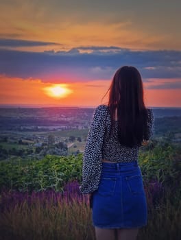 Rear view of a woman in skirt watching the sunset over the valley. Natural summer dusk scene