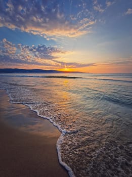 Early morning on the beach with a peaceful view to the sunrise above the sea. Calm seascape dawn scene, natural background. Summer holiday and travel concept