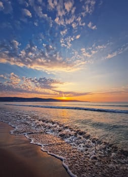 Seascape dawn scene, natural vertical background. Early morning on the beach with a peaceful view to the sunrise above the hills. Calm summer holiday, sea travel concept