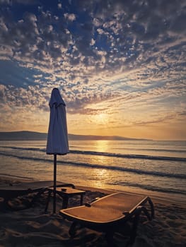 Dawn at the sea with empty beach and sunbed with umrella on the sandy beach. Summer holiday seaside, travel concept