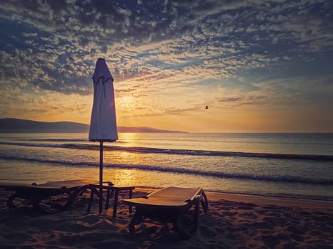 Sunrise at the sea with sunbeds and umbrella on the sandy beach. Summer holiday seaside, travel concept