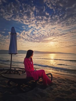 Woman relaxing on the sunbed as meets the dawn at the beach. Beautiful sea sunrise scene, summer vacation seaside, travel and holiday relaxation concept