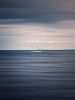 Seascape with a sailboat on the horizon, motion blur effect