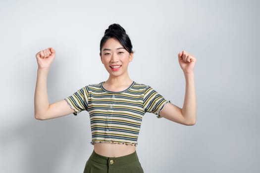 Beautiful Asian woman raises arms and fists clenched with celebrating victory expressing success.