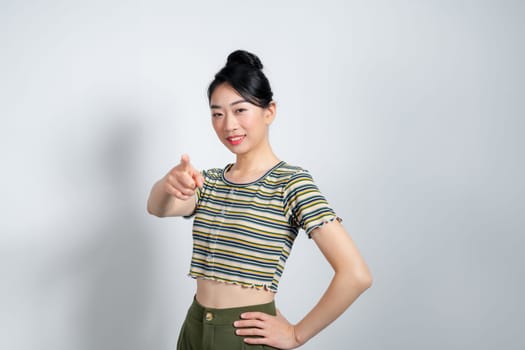 Image closeup of delighted asian woman smiling and pointing finger at camera isolated over white wall