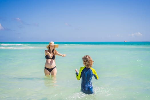 A radiant pregnant mother and her excited son share a tender moment on a serene, snow-white beach, celebrating family love amidst nature's beauty.