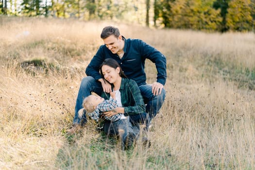 Dad sits behind mom with a little girl on her lap in a clearing. High quality photo