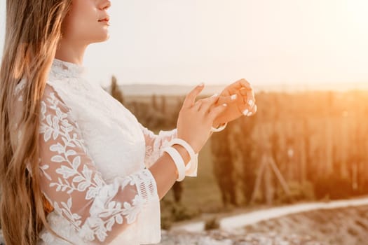 Romantic beautiful bride in white dress posing with sea and mountains in background. Stylish bride standing back on beautiful landscape of sea and mountains on sunset