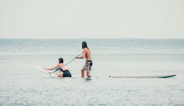 Sea woman and man on sup. Silhouette of happy young woman and man, surfing on SUP board, confident paddling through water surface. Idyllic sunset. Active lifestyle at sea or river