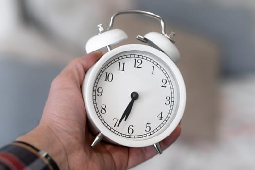 Round white alarm clock in a man's hand close-up. The hands on the clock show half past seven in the morning, time to get up. Retro alarm clock on the table, vintage tone. space for text