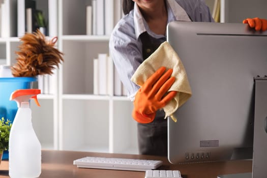 Young woman uses a cleaning cloth to disinfect the computer and equipment on the office table. Cleaning worker or housekeeper cleans the office.