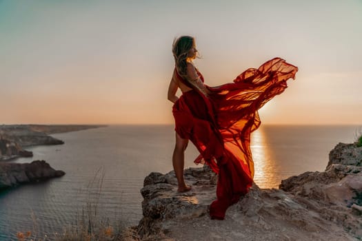 Woman sunset sea red dress, side view a happy beautiful sensual woman in a red long dress posing on a rock high above the sea on sunset