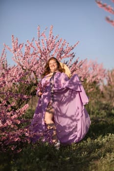 Woman blooming peach orchard. Against the backdrop of a picturesque peach orchard, a woman in a long pink dress and hat enjoys a peaceful walk in the park, surrounded by the beauty of nature