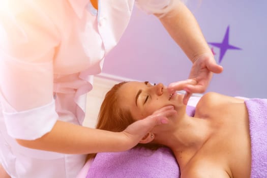 Relaxing massage. European woman getting facial massage in spa salon, side view.