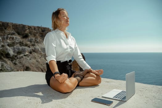 Freelance women sea working on the computer. Good looking middle aged woman typing on a laptop keyboard outdoors with a beautiful sea view. The concept of remote work