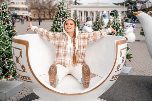 Woman Christmas Square. She sits in a large white cup, dressed in a light suit. With trees decorated with Christmas tinsel in the background.